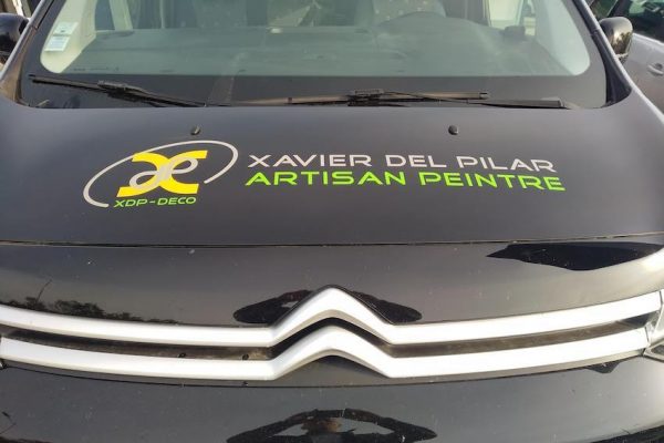 Autocollant logo et texte découpé à la forme en transfert adhésif posé sur un capot de voiture noire.