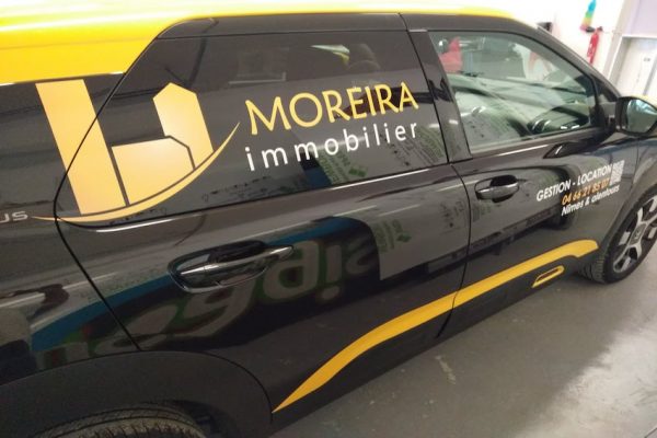 Logo Moreira immobilier en découpe sur latéral de véhicule noir.
