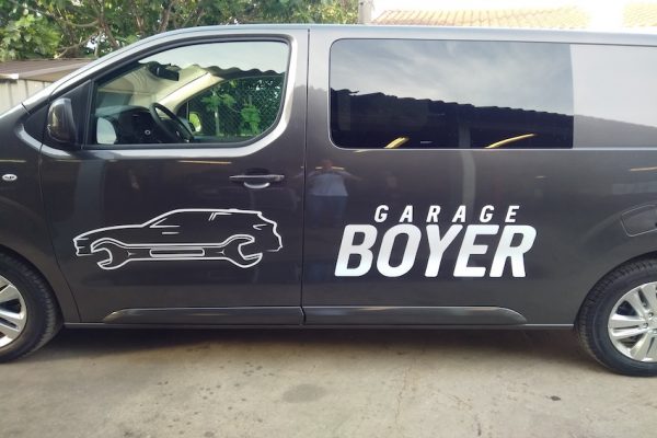 Logo blanc garage Boyer appliqué sur un latéral d'un fourgon gris anthracite.