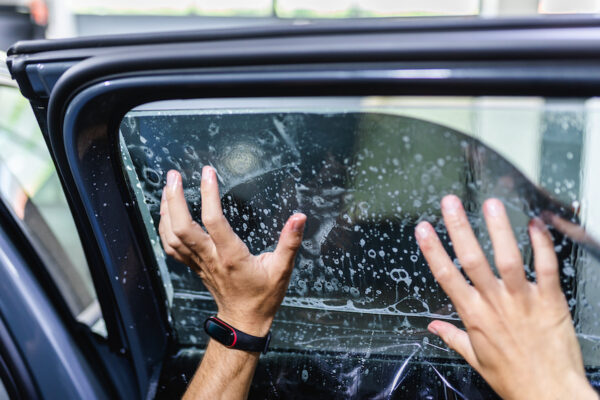 2 mains entrain de poser un film adhésif teinté sur une vitre de voiture
