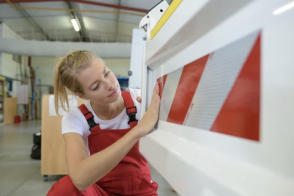 Femme posant une bande adhésive rétro-réfléchissante sur l'arrière d'un camion